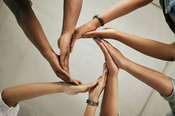 Close up of a group of colleagues putting hands together to form a circle in the office from below. Creative team joining hands and showing unity in teamwork.