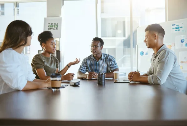 Group of diverse businesspeople having a meeting in an office at work. Happy african american businesswoman talking during a workshop at a table with coworkers. Businesspeople planning together.