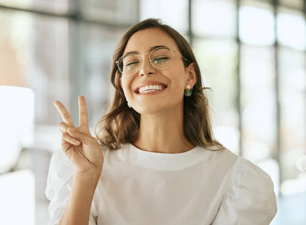 Young excited professional with glasses gesturing peace sigh. Playful business woman entrepreneur showing victory sign in an office.