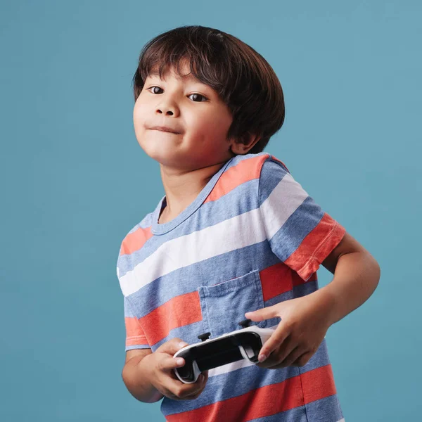 Young mixed race boy standing and holding a console controller while playing a video game against a blue background. Fun and games are a good activity for weekends.