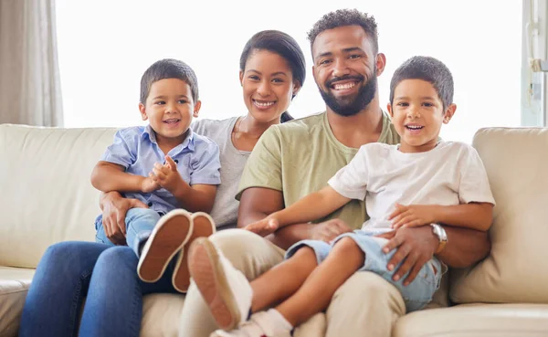 Happy young mixed race family smiling looking cheerful and relaxing on the couch together at home. Two hispanic parents enjoying a day with their little children at home one the weekend.