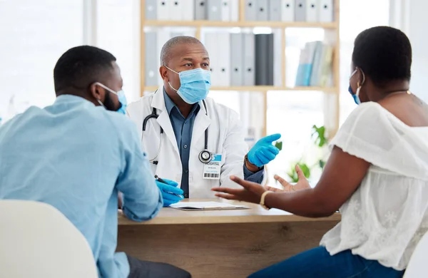 African american couple talking to a doctor about fertility treatment. Professional gp wearing a mask to protect from covid during checkup. Married couple in consult for corona.