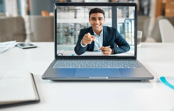 Happy mixed race businessman pointing his finger on a video call using a laptop alone at work. One hispanic businessperson smiling on a virtual call in an office.