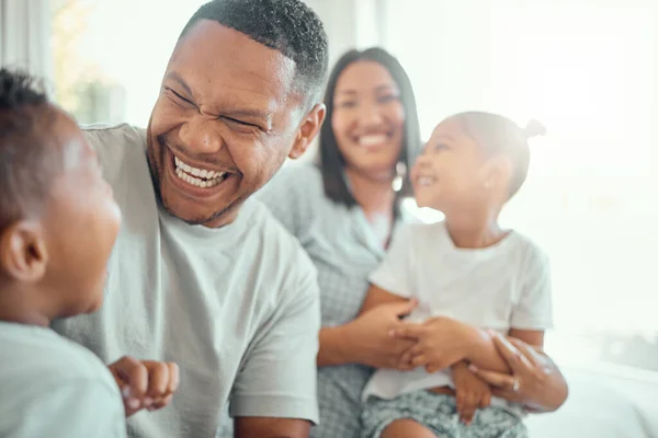 Happy funny mixed race family with two children wearing pyjamas and sitting together at home. Cheerful father laughing and playing with his son while having fun at home.