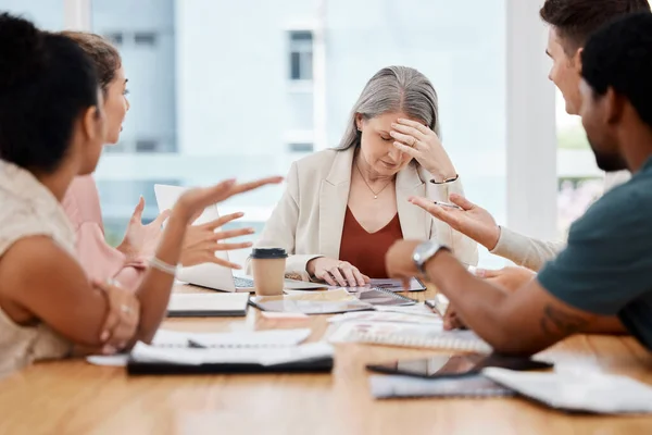Group of businesspeople having a meeting together in a boardroom at work. Stressed mature caucasian businesswoman suffering from a headache while her colleagues talk.