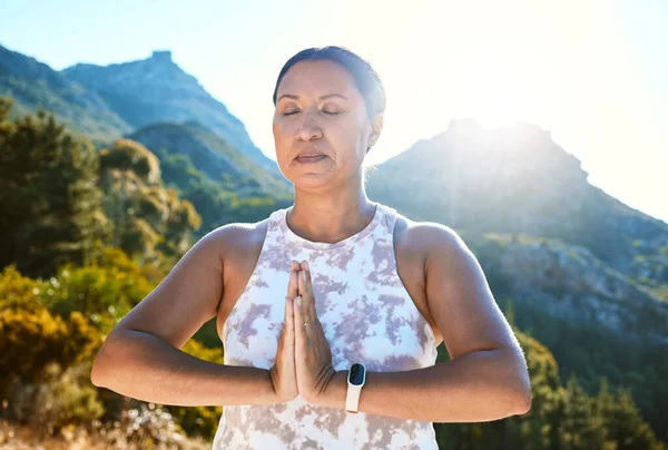 Mature woman meditating with joined hands and closed eyes breathing deeply. Finding inner peace, balance and living healthy.