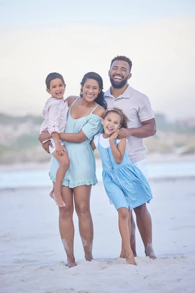 Full length portrait of a happy mixed race family standing together on the beach. Loving parents spending time with their two children during family vacation by the beach.
