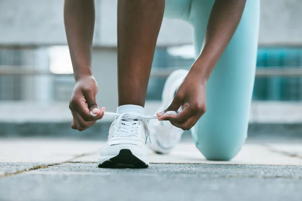 一名非洲裔美国妇女在外面锻炼时系鞋带的衣服 黑色运动员紧固运动鞋 以适应舒适的身体 并防止在训练时绊倒 — 图库照片