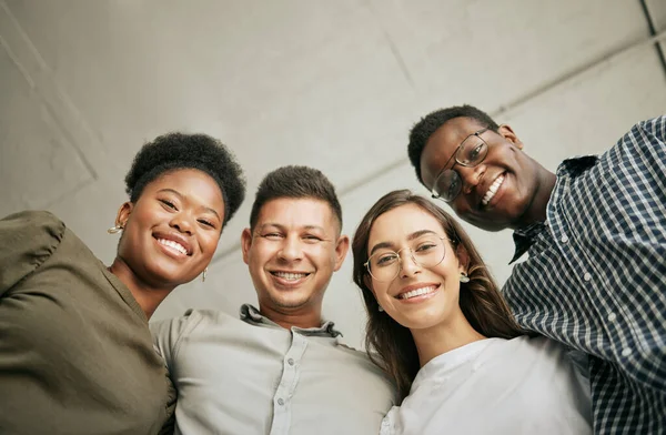 Portrait of happy united young business team hugging each other. Diverse mixed race group of men and women standing in row in their office, huddling and smiling all together.