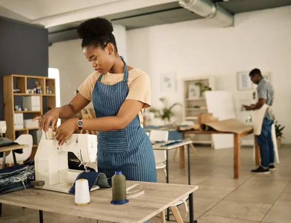 fashion designer threading needle on a sewing machine. Young tailor using sewing machine. Seamstress getting her sewing machine ready. African American designer working in a studio.