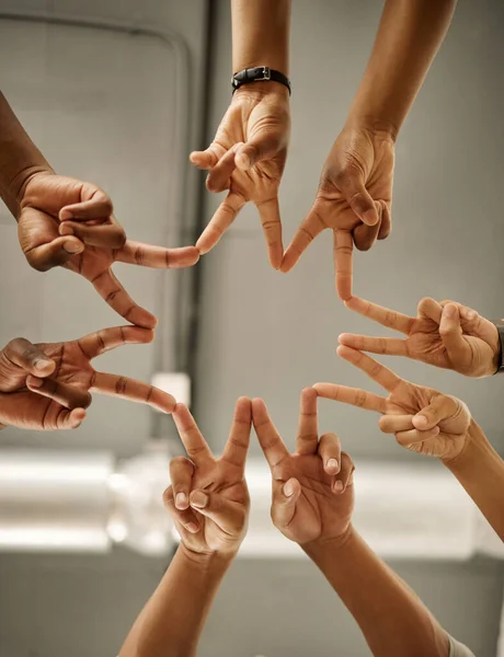 Closeup of hands of coworkers making peace signs in a star shape. Colleagues forming peace signs from below. Group of businesspeople collaborating together. Businesspeople joined together in unity.
