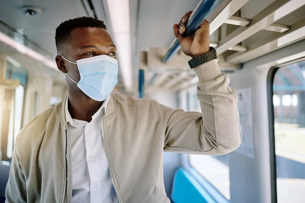 Black businessman travelling alone and standing on a train on his way to work in the morning. African american male wearing a mask on his commute to the city.