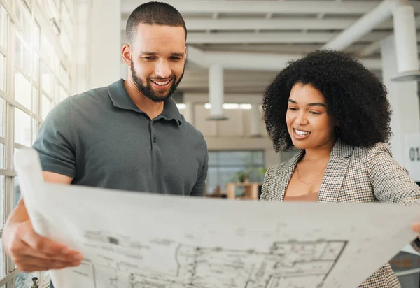 Young coworkers looking at a blueprint. Two businesspeople collaborate on a building plan. Design creatives working together in a modern office. Happy colleagues plan a building project together.