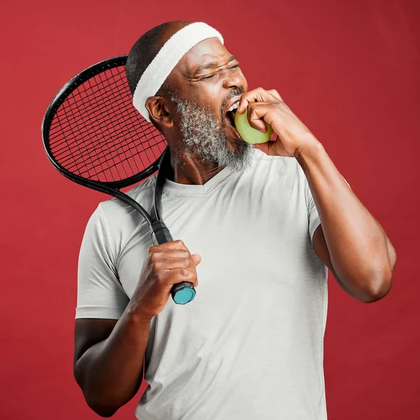 One happy mature african american man standing against a red background in studio and posing with a tennis racquet. Smiling black man feeling fit and sporty while playing a match. Ready for the court.