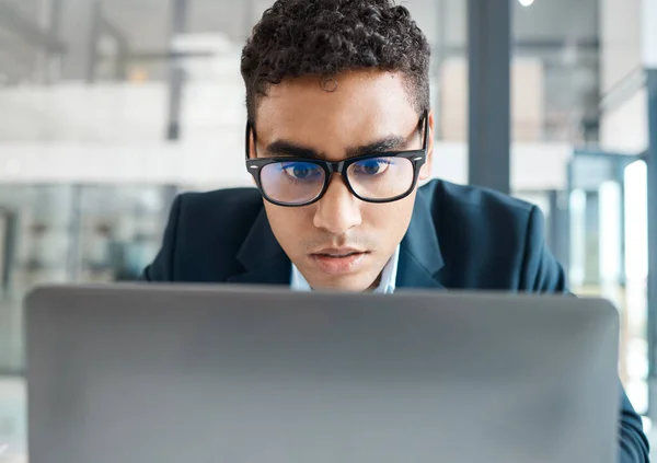 Serious mixed race businessman working on a laptop alone at work. Face of a focused hispanic male businessperson reading an email on a laptop while working in an office.