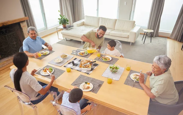 Overhead view of a mixed race family sitting at a table having lunch in the lounge at home. Hispanic grandparents having a meal with their kids and grandkids at home.