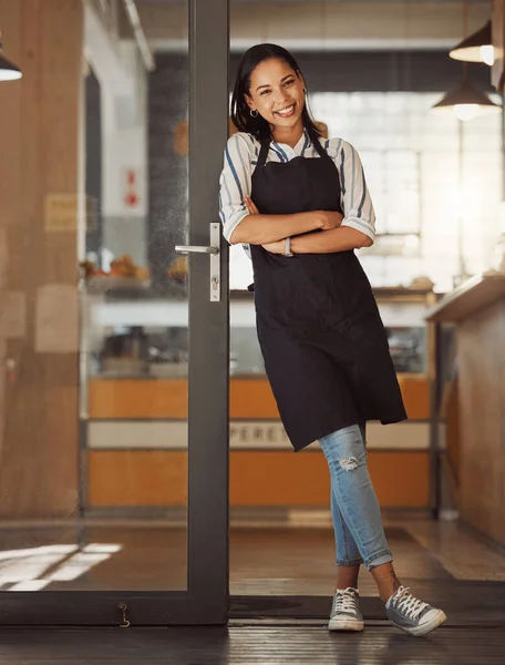 Portrait of confident businesswoman leaning on her business door. Young boss arms crossed in her store entrance. Business assistant standing in her cafe entrance. small business owner in her store.