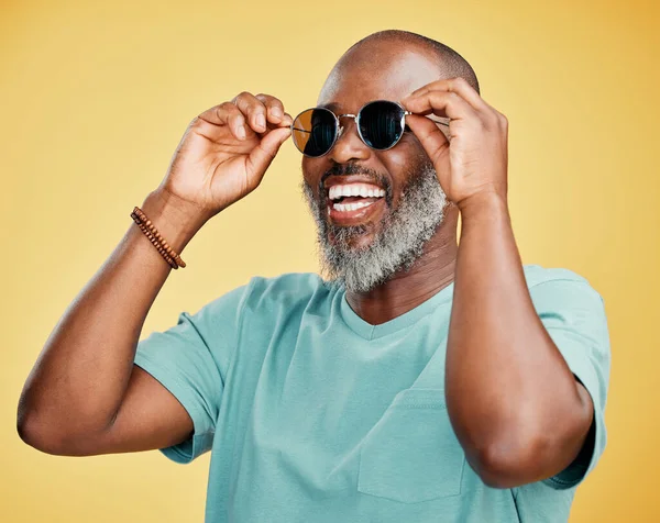 Happy mature African American man standing alone against yellow background in a studio and posing with sunglasses. Smiling black man feeling fashionable and cool while wearing glasses. Summer ready.