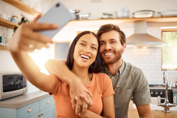 Young content interracial couple taking a selfie with a phone together at home. Joyful mixed race girlfriend taking a photo with her caucasian boyfriend on a cellphone. Happy husband and wife relaxin.