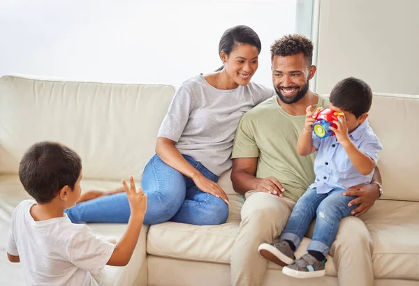 Young mixed race family bonding in the lounge while the parents relax on the couch while their two little sons play. Hispanic couple smiling while watching their boys playing in the living room.