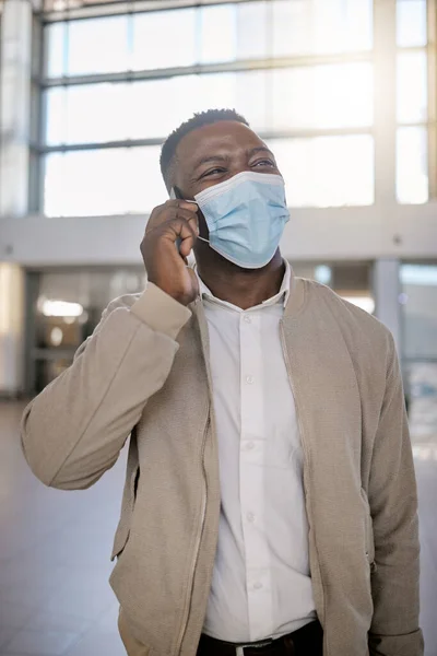 African american male on a phone call with his mobile device inside a station during the day while wearing a mask. Young black male talking on a phone while commuting in a train station.