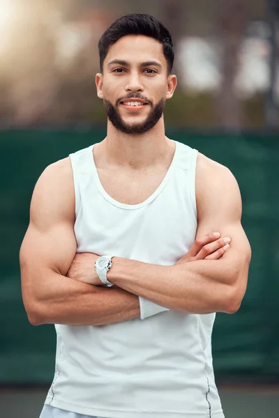 Portrait of smiling mixed race tennis player with arms folded and standing alone on court. Fit confident hispanic sports professional with arms crossed in sports club. Ready for athletic healthy game.