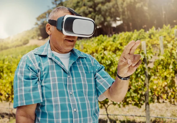 One senior mixed race farmer using a virtual reality headset through metaverse. Hispanic elderly man touching augmented reality in multiverse. Old man standing alone and using vr for a simulation.