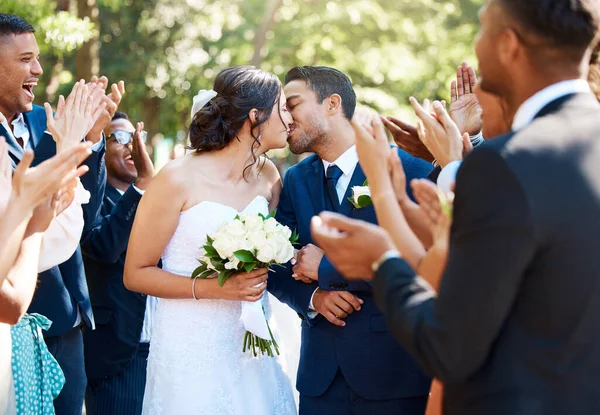 Bride and groom kissing after wedding ceremony while friends and family clap and celebrate their wedding day.