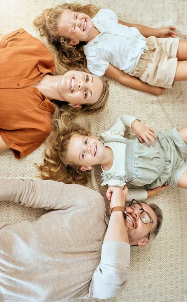 A happy Caucasian family of four lying in the living room at home. Loving smiling family being affectionate on the lounge floor. Young couple bonding with their little kids at home.
