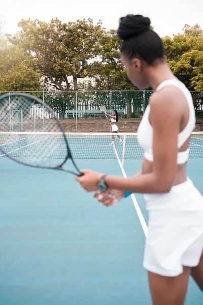 Young woman serving during a tennis match. Two women playing a game of tennis together. African american athletes enjoying a practice match of tennis. Women standing on the court.