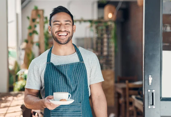 Portrait of one young hispanic waiter serving a cup of coffee while working in a cafe. Friendly barista and coffeeshop owner managing a successful restaurant startup.
