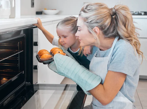 Young mother smelling a tray of fresh baked muffins. Caucasian woman sniffing a tray of muffins. Mother and daughter removed fresh baked muffins from the oven. Woman enjoying the smell of muffins.