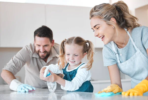 Little girl spraying the kitchen counter. Caucasian family cleaning the kitchen together. Happy family doing chores together. Cheerful family disinfecting the kitchen counter together.