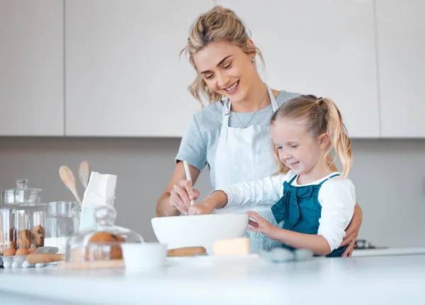 Happy mother helping her daughter bake. Parent baking with her child. Young woman helping her daughter make batter. Little girl mixing a bowl of batter. Smiling family baking in the kitchen.