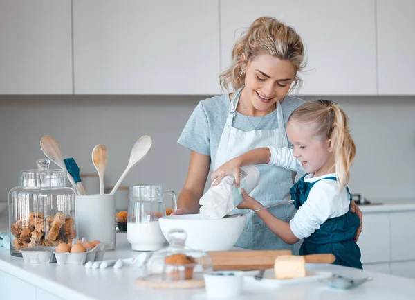 Little girl pouring flour into a bowl. Young child sifting flour into a bowl. Happy mother helping her daughter bake. Caucasian mother baking with her daughter in the kitchen. Family baking together.