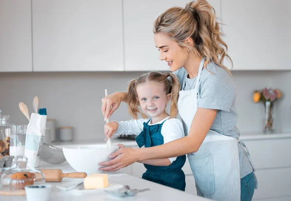 Portrait of a little girl baking with her mother. Happy mother helping her daughter bake. Parent baking with her child in the kitchen.Mother helping her daughter bake at the kitchen counter