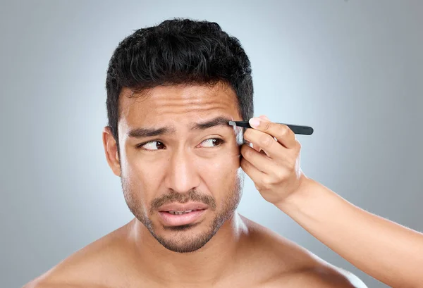 Shaping your brows isnt exactly painless. a handsome man getting his eyebrows tweezed