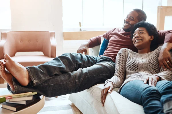 Couple, relax and watching tv on a sofa, happy and smile while bonding in their home together. Television, resting and black woman with man on a sofa, resting and having fun in the living room.