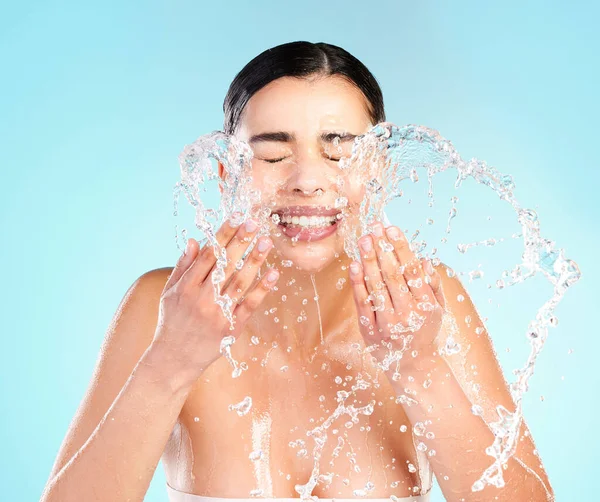 Beauty has no skin tone. a beautiful young woman being splashed with water in the face against a blue background