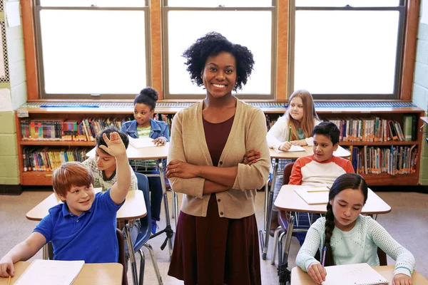 Portrait, teacher and education with a black woman in a classroom, standing arms crossed with her students. School, learning or study with a female educator in a class with a boy and girl pupils.