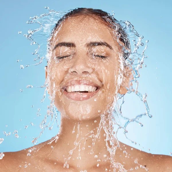 Laughing woman, washing face or water splash skincare in relax healthcare wellness or grooming hygiene cleaning on blue background studio. Smile, beauty model or wet water drops in facial dermatology.