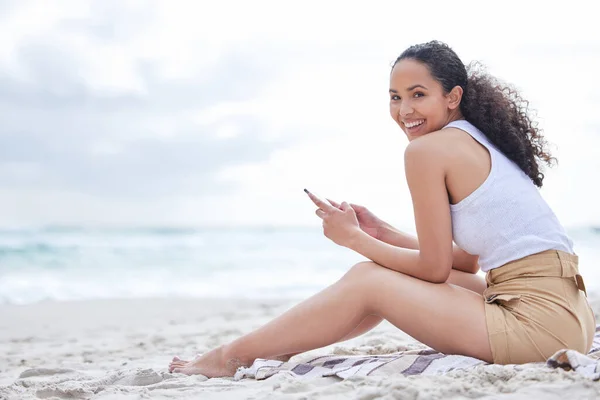 I always stay connected. a young woman using a phone at the beach