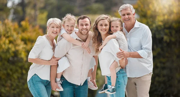Portrait of multi-generation family standing together. Extended caucasian family smiling while spending time together at the park on a sunny day. Family with two children, parents and grandparents.