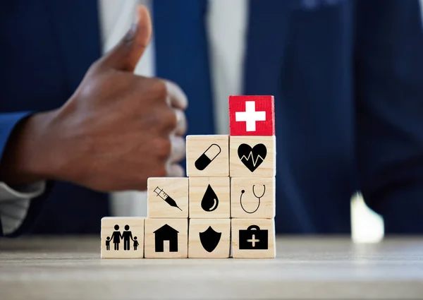 Whatever happens, weve got you covered. an unrecognisable businessman assembling wooden blocks with insurance related symbols on them and showing thumbs up