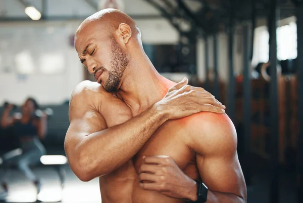 I barely feel pain, but this is unbearable. a muscular young man holding his shoulder in pain while exercising in a gym