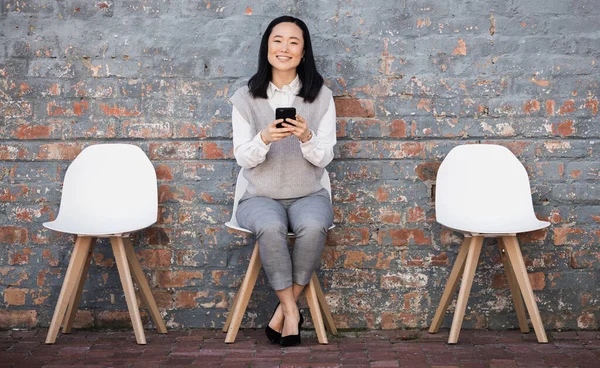 Woman waiting for interview on chair with phone, recruitment and employment with smile. Portrait of happy person in Japan sitting on chair, smiling and excited for job opportunity for Japanese people.