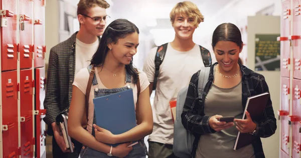 A well prepared future is on its way. a group of teenagers walking down the hall and using a smartphone at high school