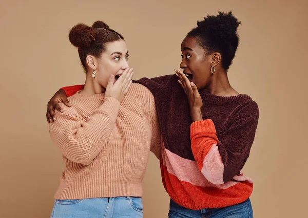 Gossip, friends and surprise face of young women with a secret and brown studio background. Wow, student surprised and girl chat together with whisper and excited discussion with shock from story.