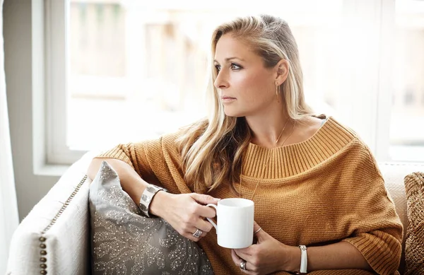 Woman, thinking and relax with coffee on sofa in living room for morning mindfulness peace, calm vision and planning lifestyle ideas in home. Female, thoughtful mindset and drinking warm tea on couch.