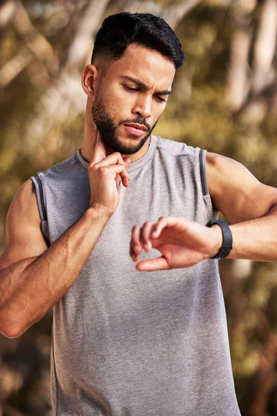 Focusing on those beats per minute. a handsome young man standing alone outside and using his watch to time his pulse after a run